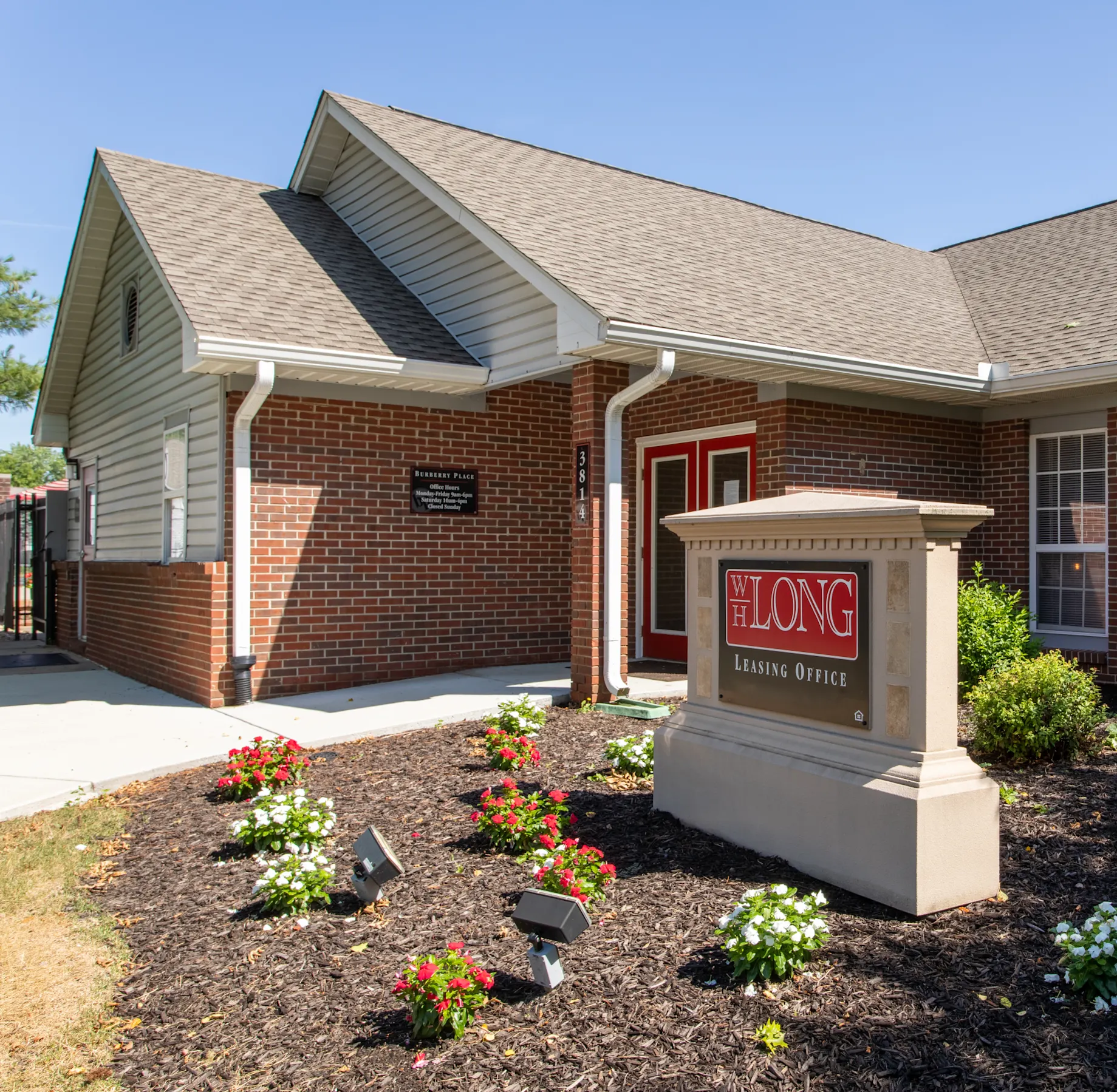 A brick leasing office building with a sign reading "WH Long Leasing Office" and landscaped flowers in front.